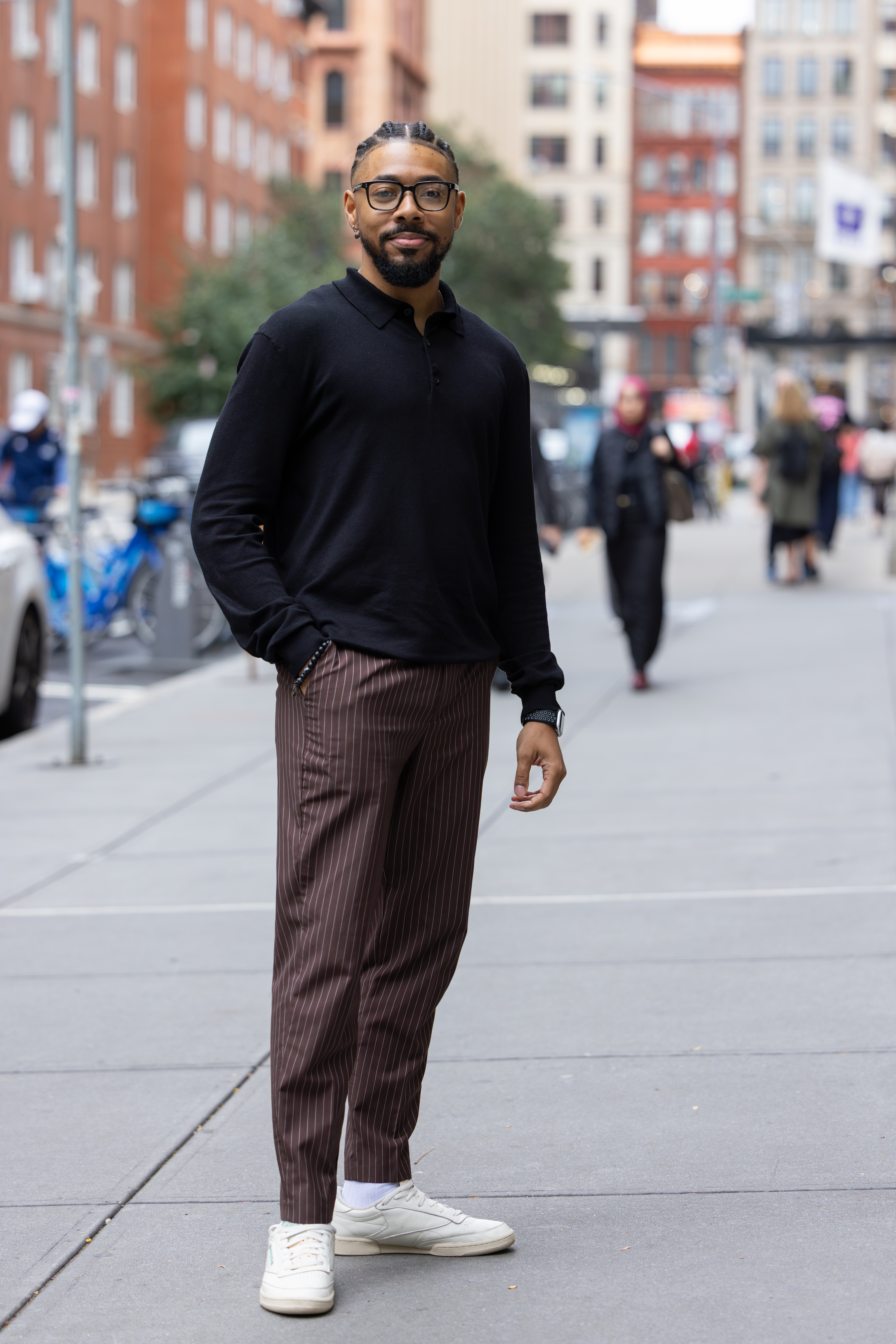 man stands on sidewalk of busy city street. tall buildings and people are in the background