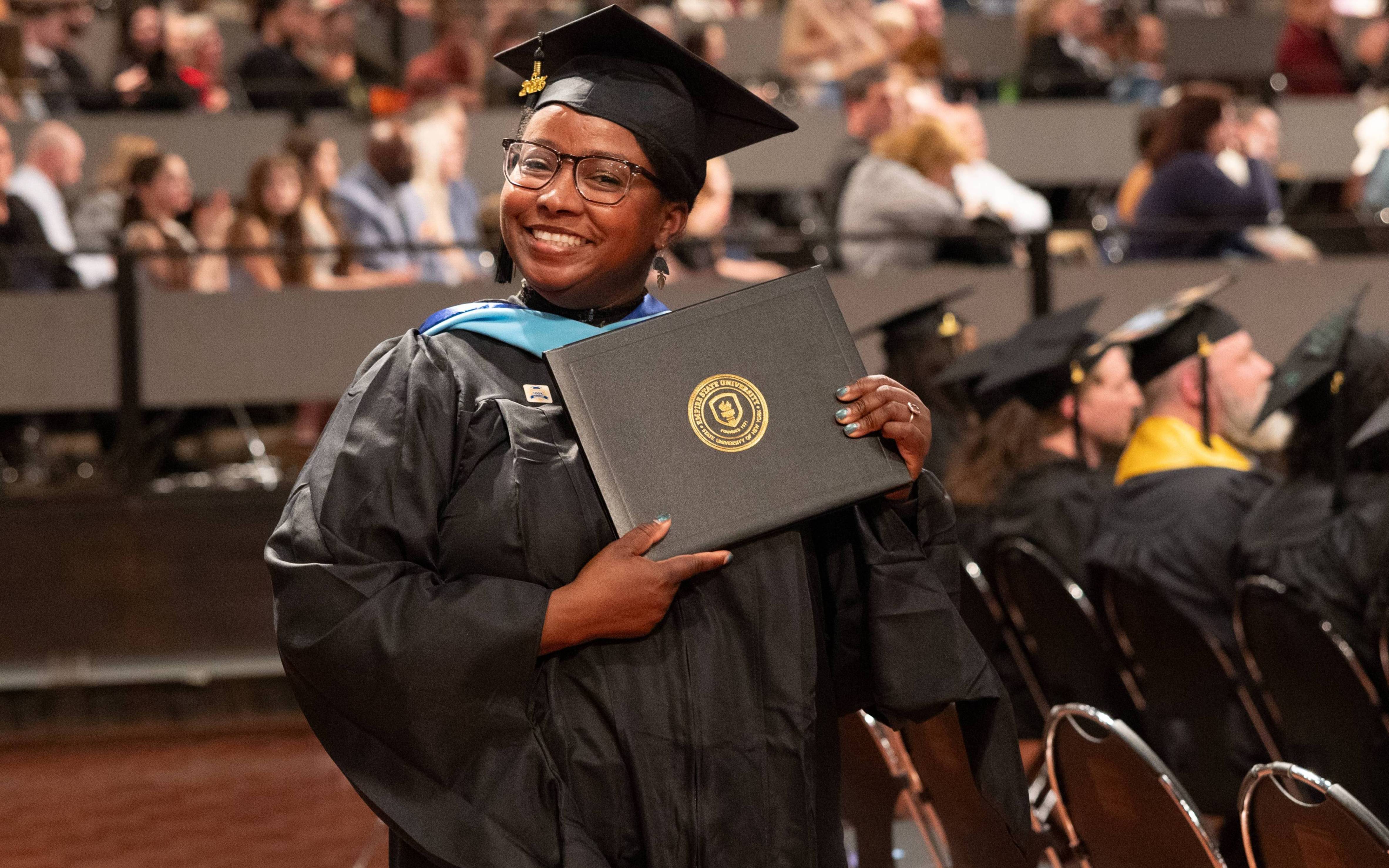Student in graduate regalia holding a diploma cover