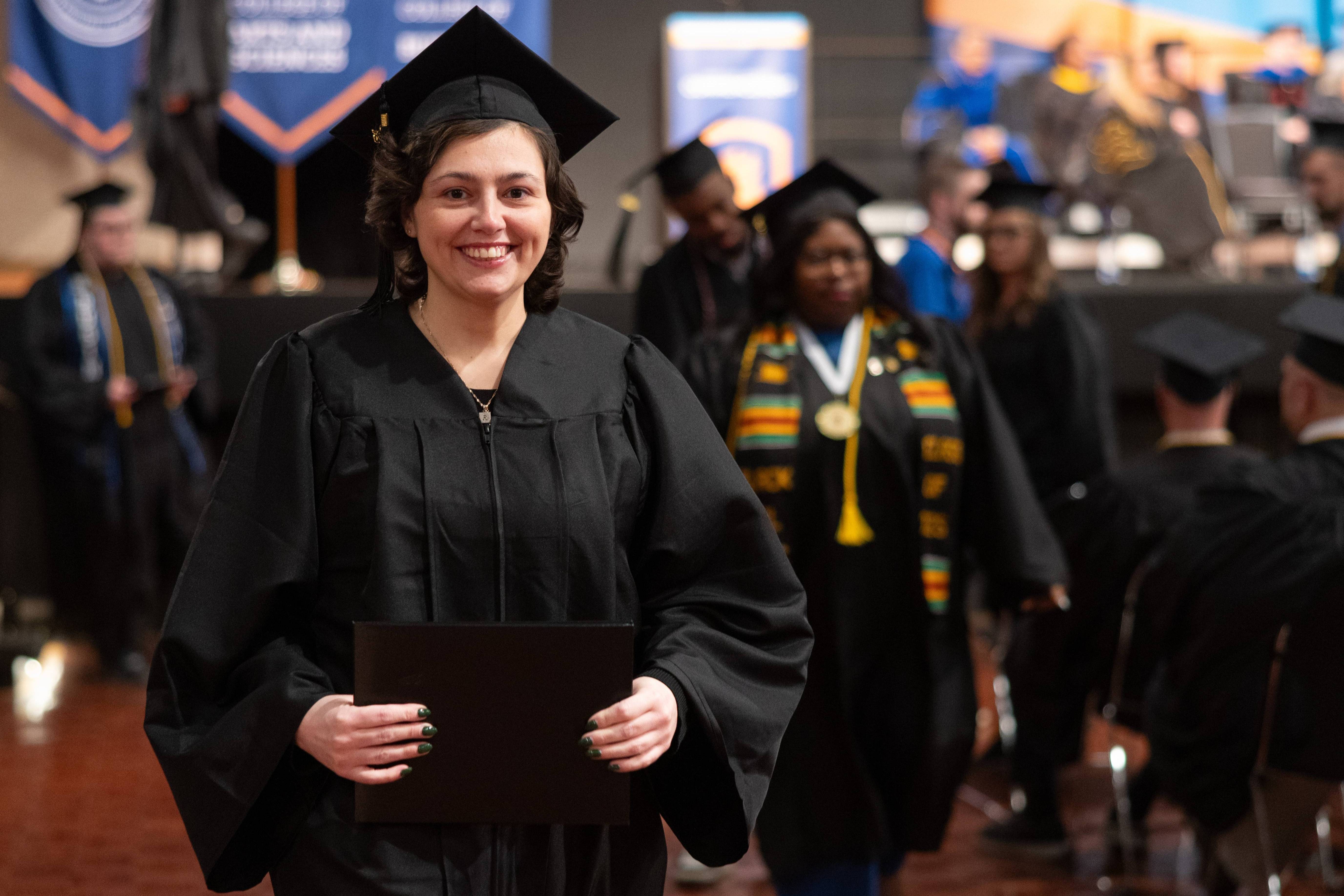Student walking in matte black regalia including mortarboard and gown.