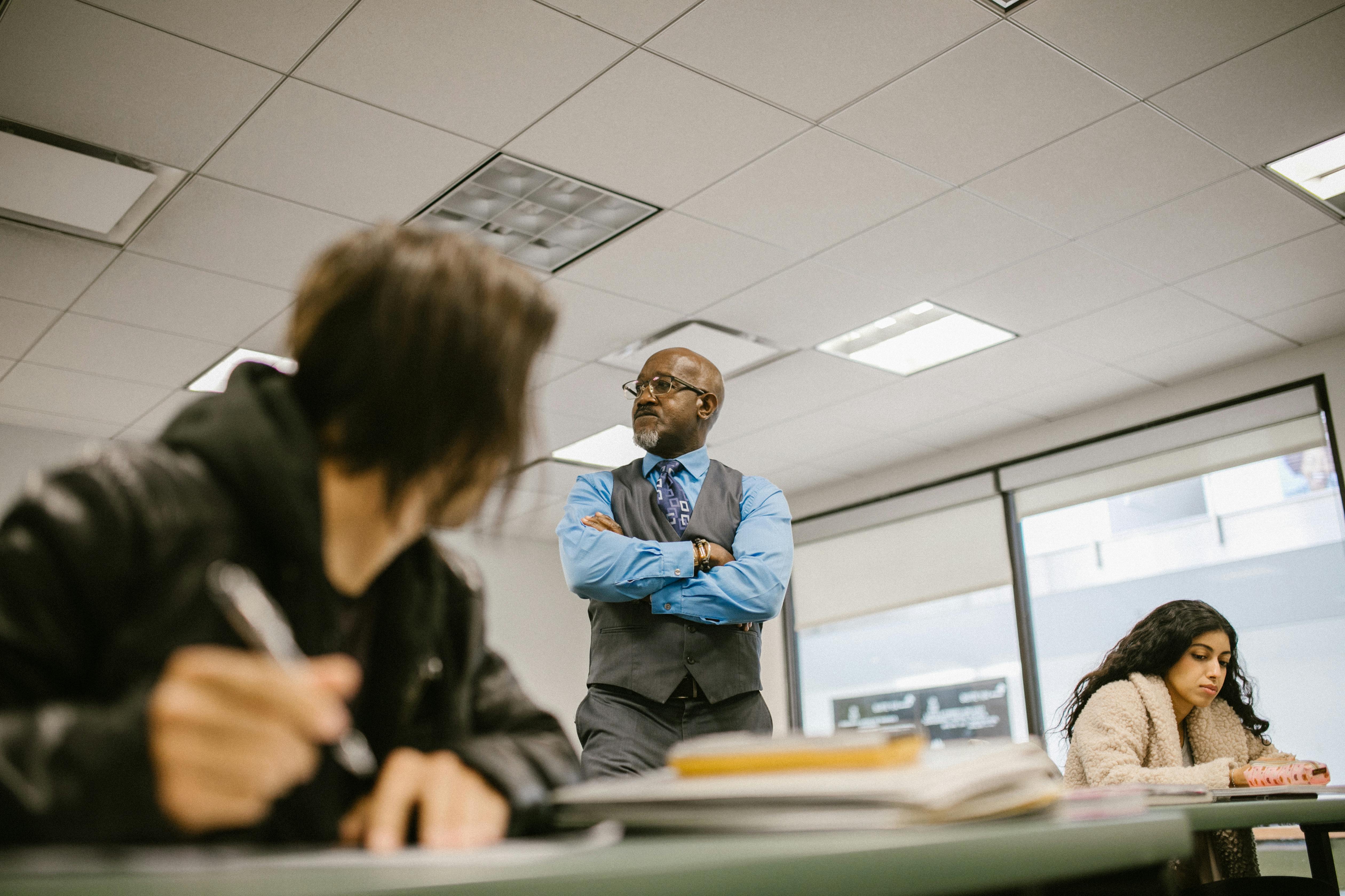 A teacher stands in the middle of the classroom as a student looks back at him.